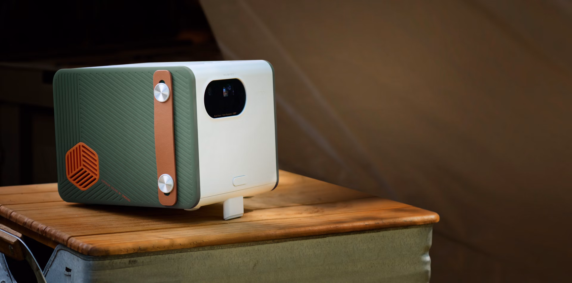 BenQ GS50 front three-quarter view in white with green sides, a tan carry strap and orange speaker cover, sitting on a wooden table