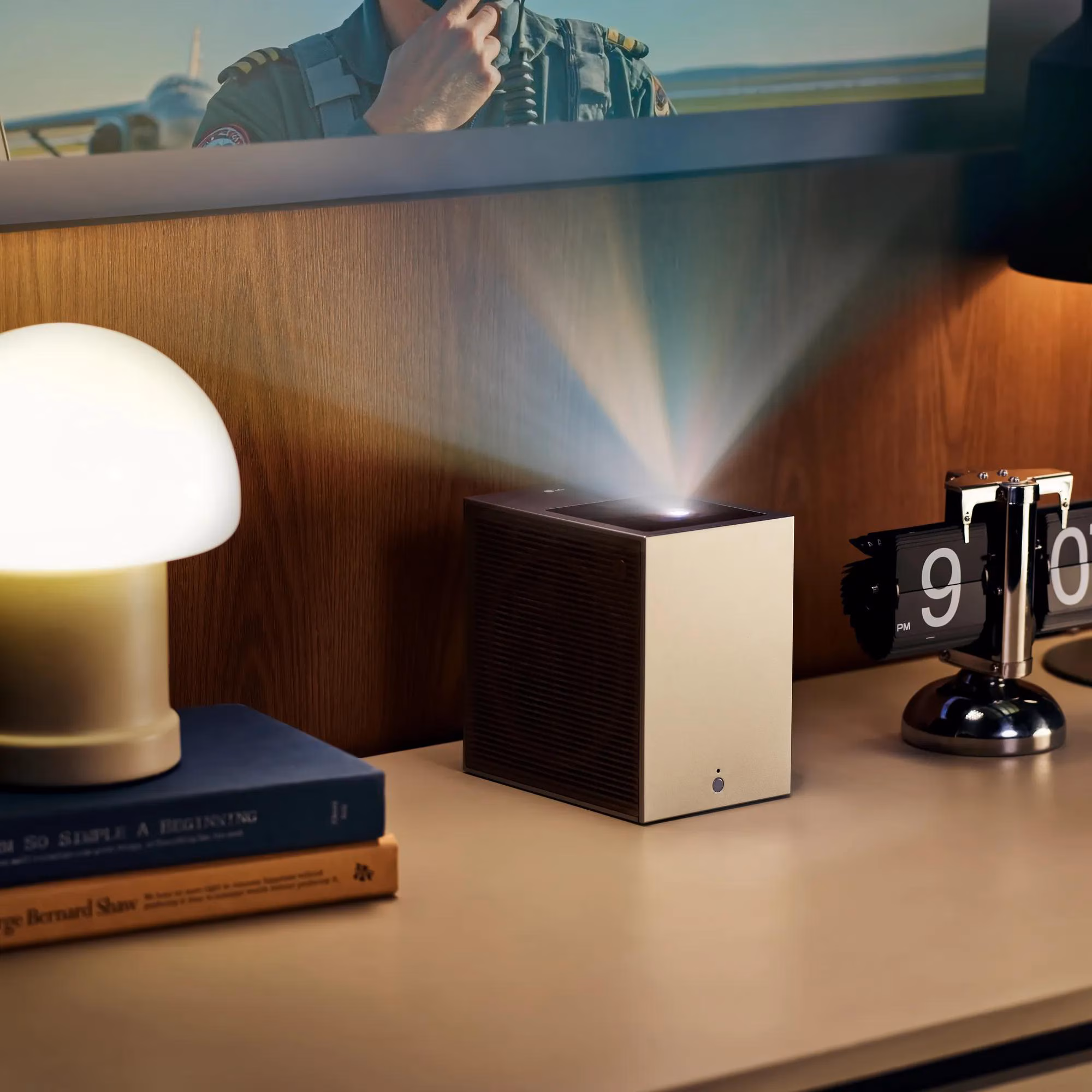 LG CineBeam S PU615U cube projector on a wooden shelf casting a beam up onto the wall, front three-quarter view