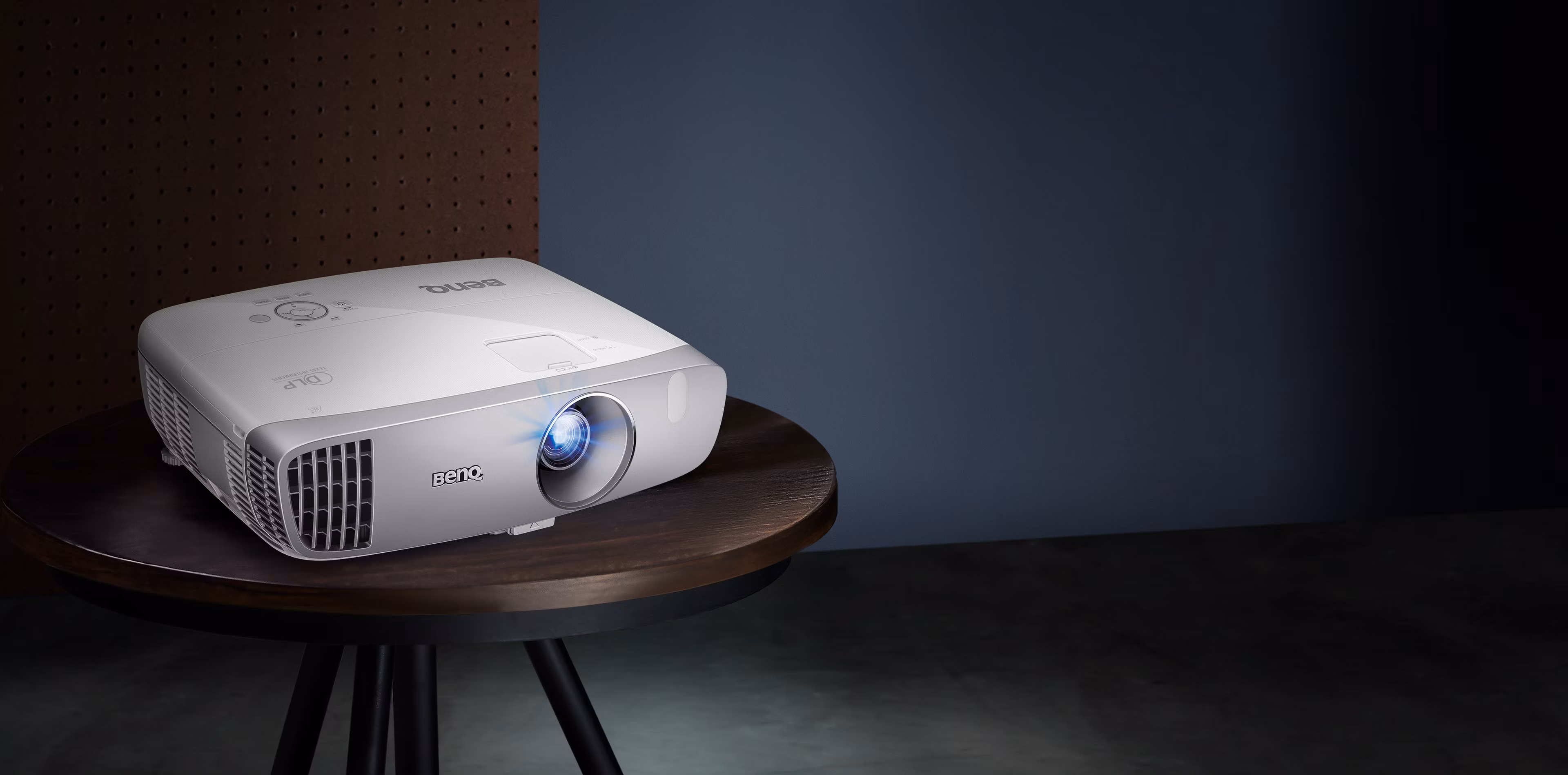 BenQ HT2050A white projector on a dark round table, front three-quarter view with the lens lit